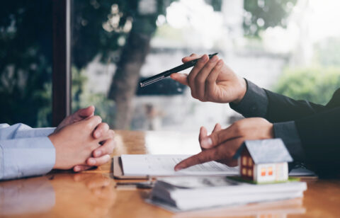 Financial professional discussing paperwork with a client at a desk with a small model house in the foreground.