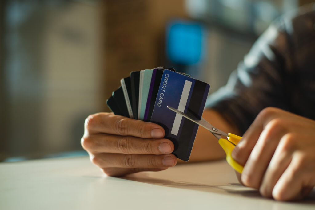 Person holding several credit cards while cutting one with scissors.