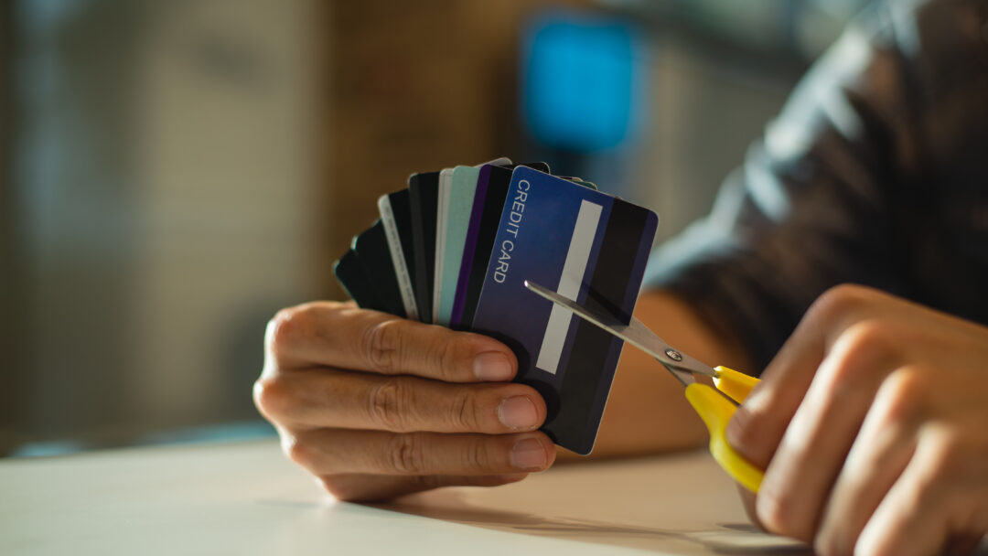 Person holding several credit cards while cutting one with scissors.