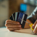 Person holding several credit cards while cutting one with scissors.