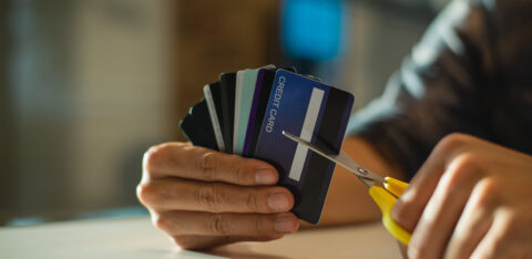 Person holding several credit cards while cutting one with scissors.