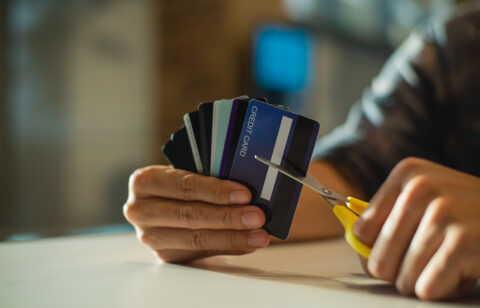 Person holding several credit cards while cutting one with scissors.