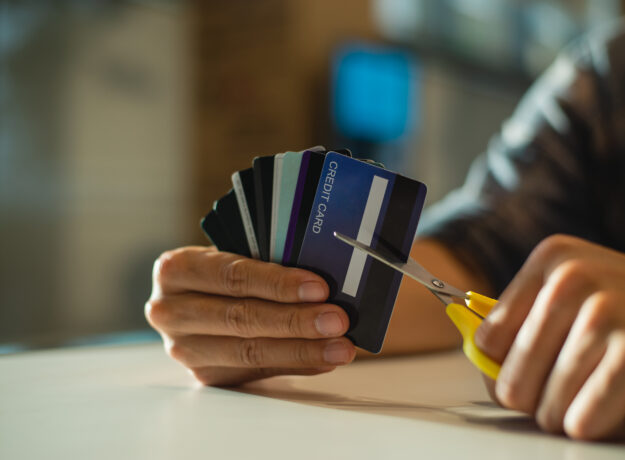 Person holding several credit cards while cutting one with scissors.