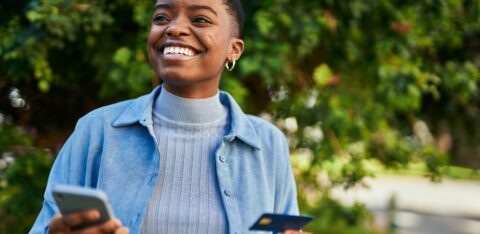 Young african american woman smiling happy holding smartphone and credit card at the city