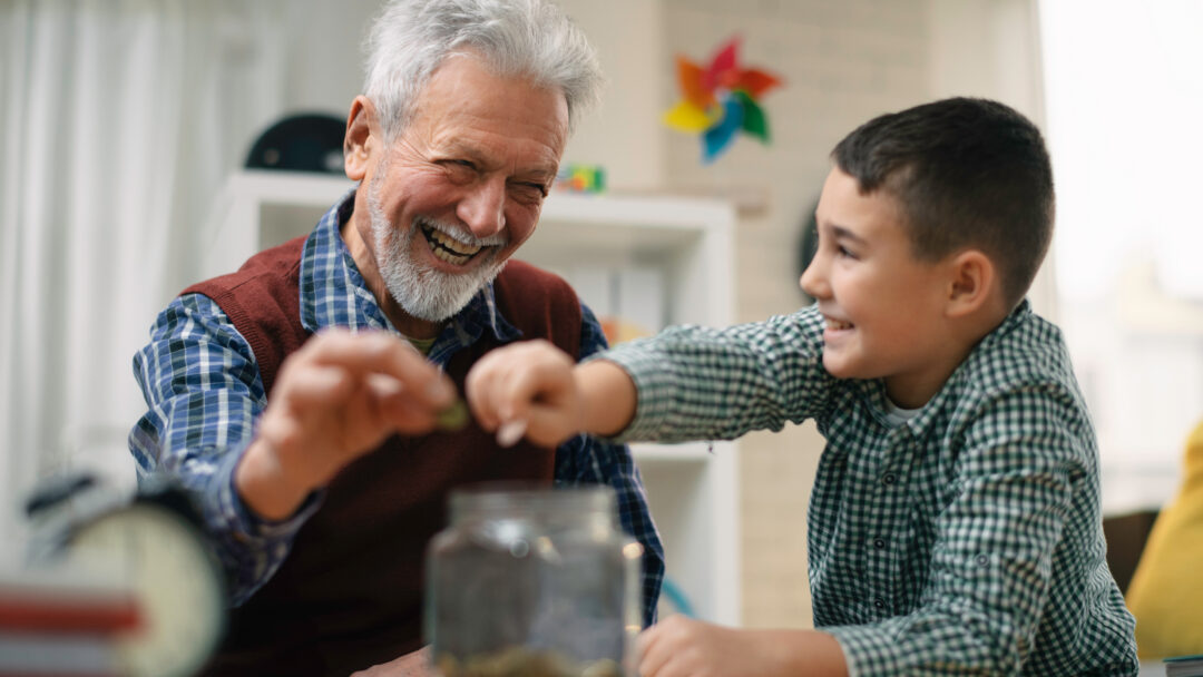 Grandpa and grandson saving money. Grandfather teaching grandchild how to save money.