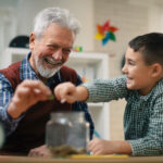 Grandpa and grandson saving money. Grandfather teaching grandchild how to save money.