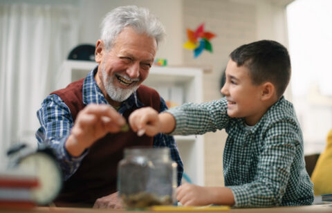 Grandpa and grandson saving money. Grandfather teaching grandchild how to save money.