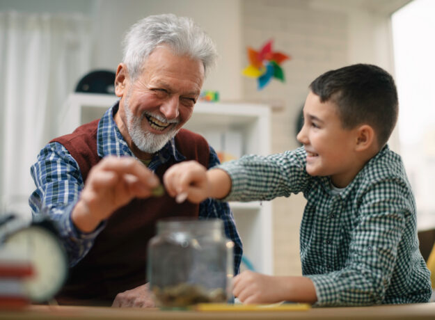 Grandpa and grandson saving money. Grandfather teaching grandchild how to save money.
