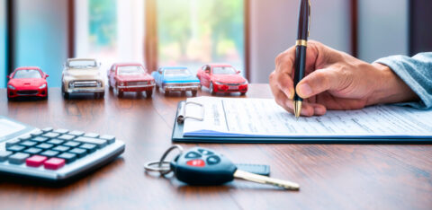 Man signing contract on car loan application form. Car loan or buying a new car concept. Miniature cars and car key on table.