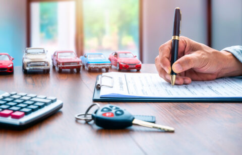 Man signing contract on car loan application form. Car loan or buying a new car concept. Miniature cars and car key on table.