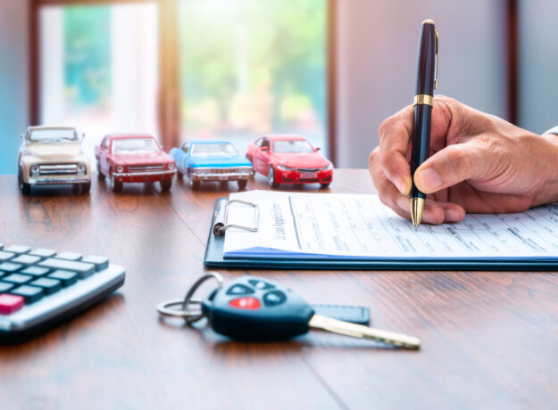 Man signing contract on car loan application form. Car loan or buying a new car concept. Miniature cars and car key on table.