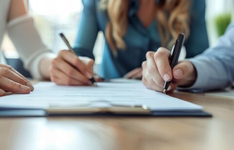 A person signing document with pen and cell phone