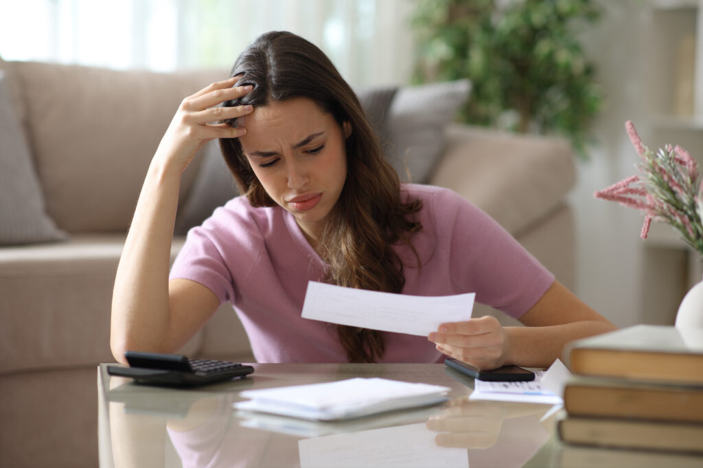 Worried woman reviewing a bill at home with a calculator and paperwork.