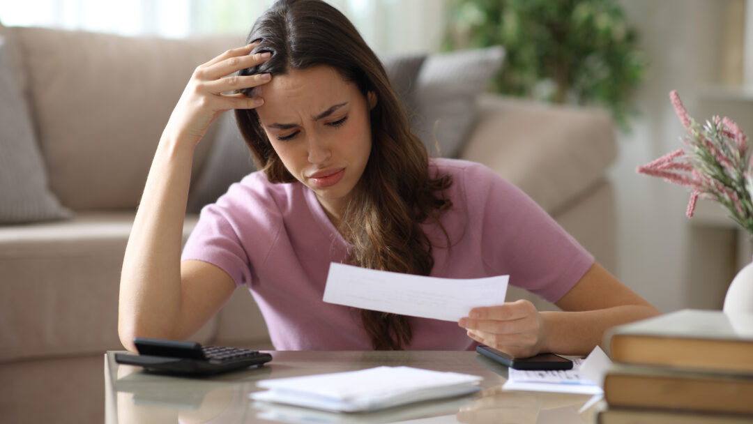 Worried woman reviewing a bill at home with a calculator and paperwork.
