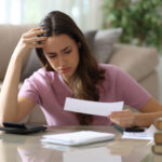 Worried woman reviewing a bill at home with a calculator and paperwork.