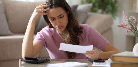 Worried woman reviewing a bill at home with a calculator and paperwork.