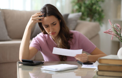 Worried woman reviewing a bill at home with a calculator and paperwork.