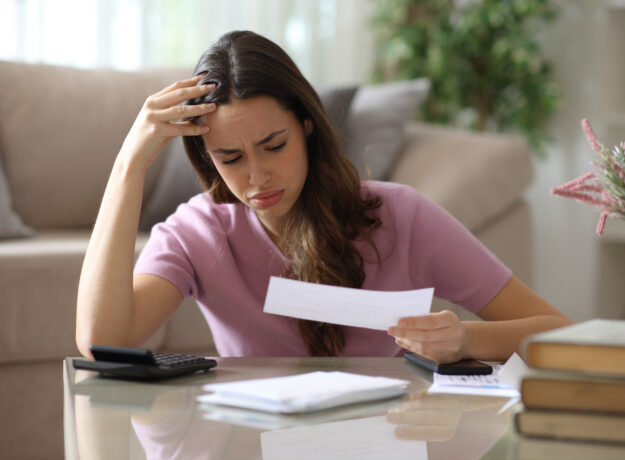 Worried woman reviewing a bill at home with a calculator and paperwork.