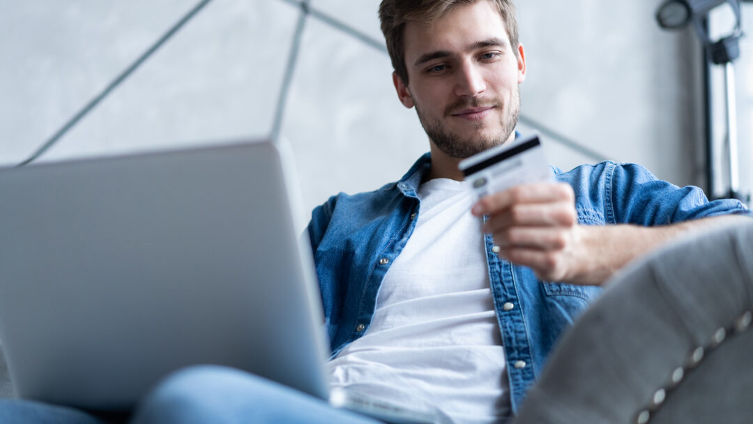 Man holding a credit card while shopping online on a laptop.