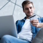 Man holding a credit card while shopping online on a laptop.