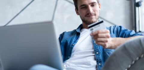 Man holding a credit card while shopping online on a laptop.