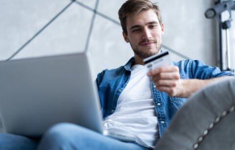 Man holding a credit card while shopping online on a laptop.