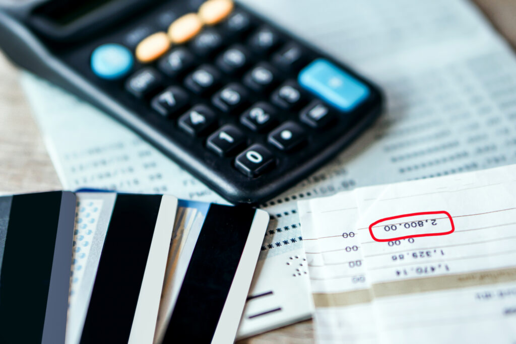 Credit cards, a calculator, and bills on a table, with a balance amount highlighted on a financial statement.