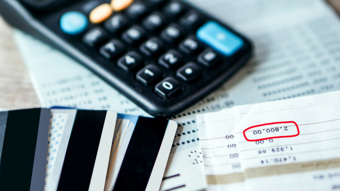 Credit cards, a calculator, and bills on a table, with a balance amount highlighted on a financial statement.