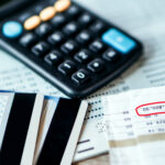 Credit cards, a calculator, and bills on a table, with a balance amount highlighted on a financial statement.