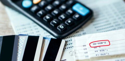 Credit cards, a calculator, and bills on a table, with a balance amount highlighted on a financial statement.