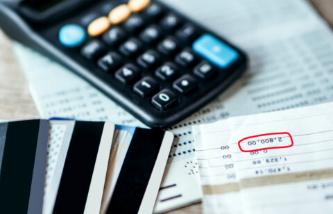 Credit cards, a calculator, and bills on a table, with a balance amount highlighted on a financial statement.