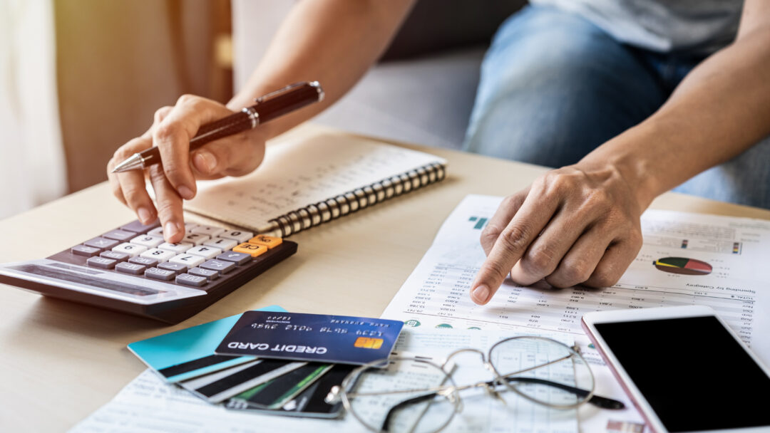Person reviewing financial documents and using a calculator beside several credit cards.