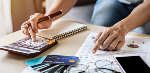 Person reviewing financial documents and using a calculator beside several credit cards.