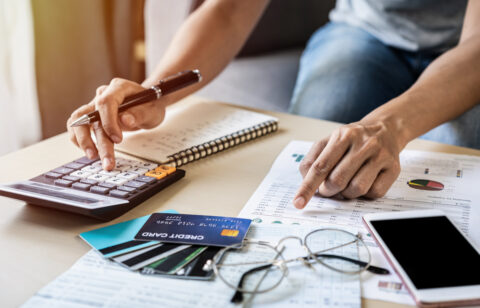 Person reviewing financial documents and using a calculator beside several credit cards.