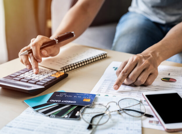 Person reviewing financial documents and using a calculator beside several credit cards.
