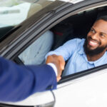 Man Sitting Inside Of New Car And Shaking Hands With Salesman