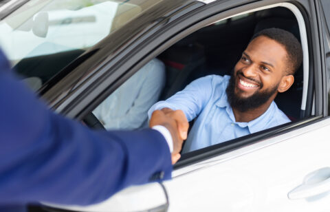 Man Sitting Inside Of New Car And Shaking Hands With Salesman