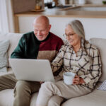 Senior couple sitting on sofa and shopping online with laptop.