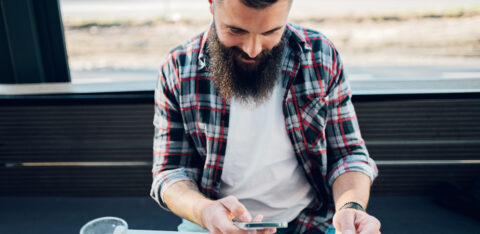 Bearded man using smartphone and a credit card in a cafe or restaurant