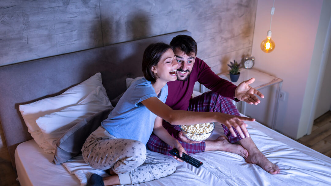 Couple watching a movie and eating popcorn in bed