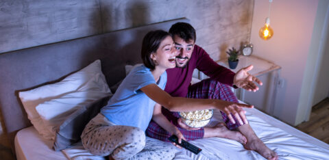 Couple watching a movie and eating popcorn in bed