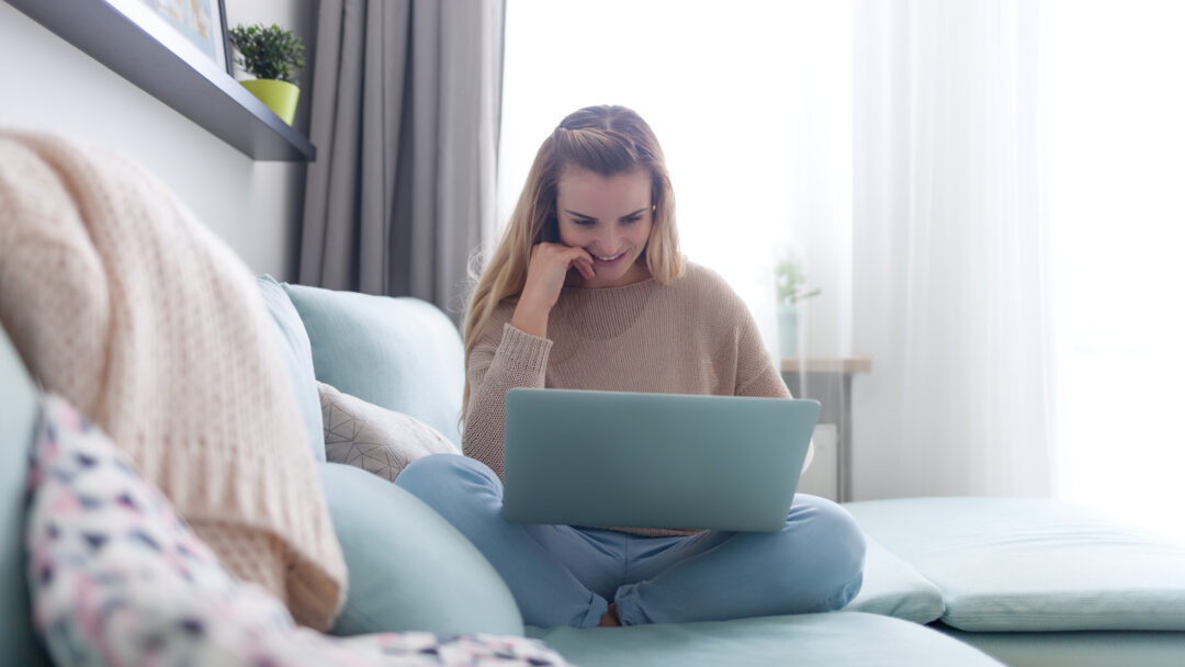 Happy woman at home using laptop sitting on sofa, online working