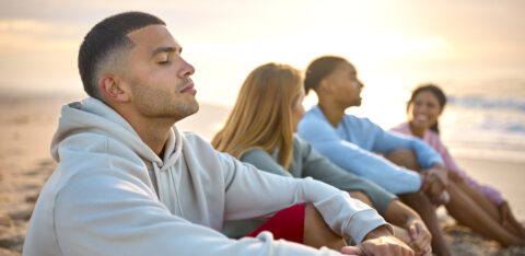 Man With Closed Eyes Relaxing With Friends On Vacation Sitting on beach thinking bout financial independence