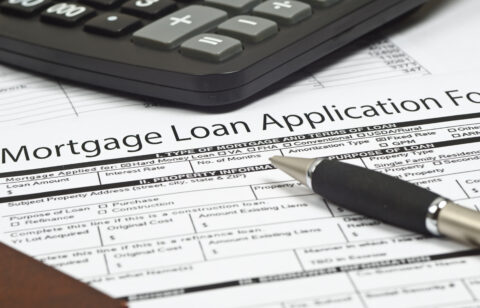 Close-up of a mortgage loan application form with a pen and calculator on top.