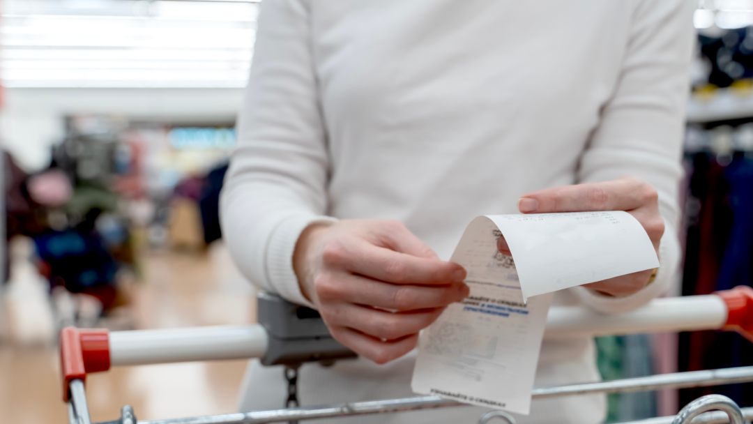 Person standing by shopping cart while looking at grocery bill