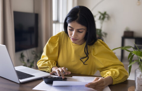 Woman in yellow shirt looking at calculator and paper