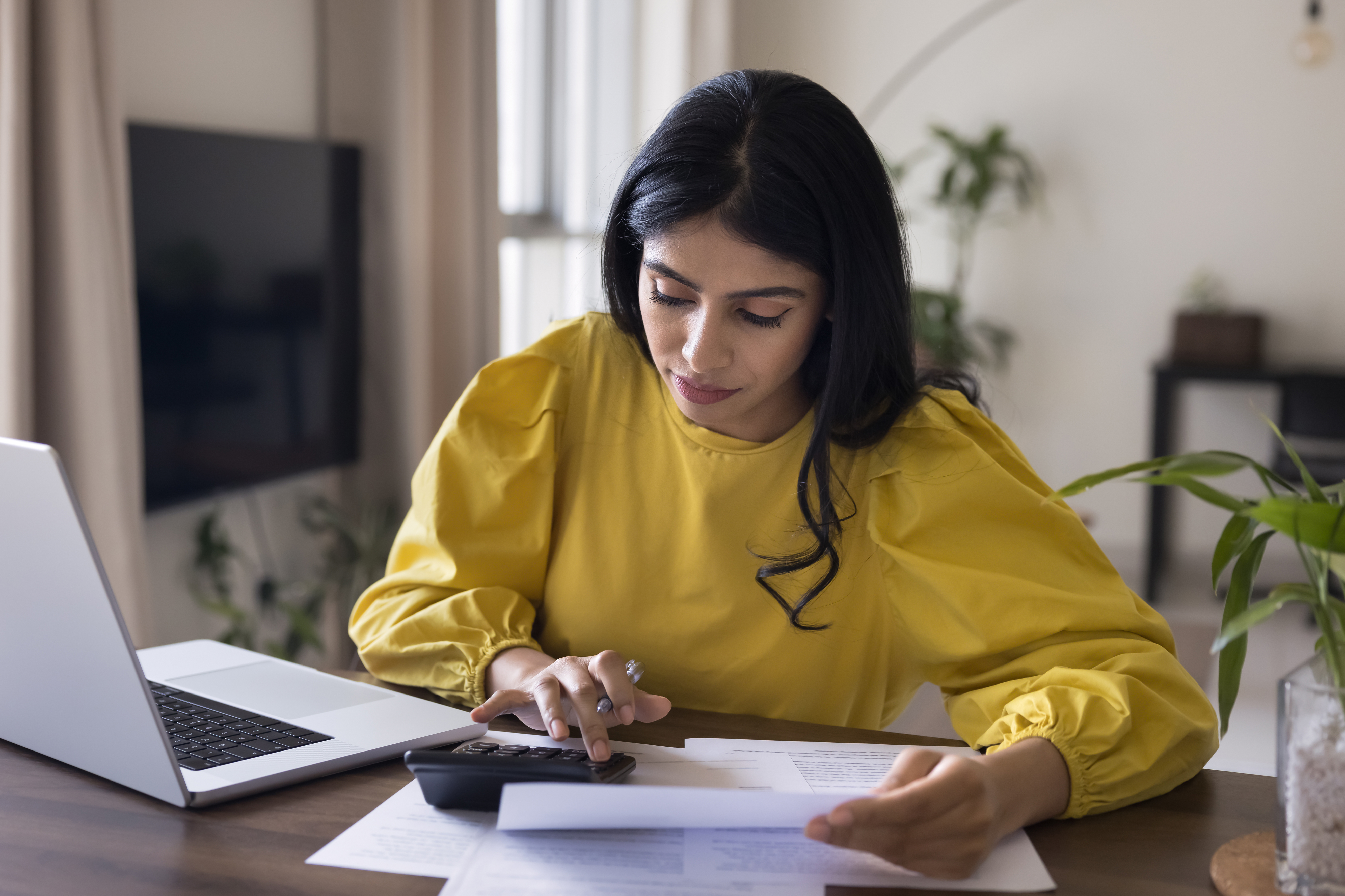 Woman in yellow shirt looking at calculator and paper