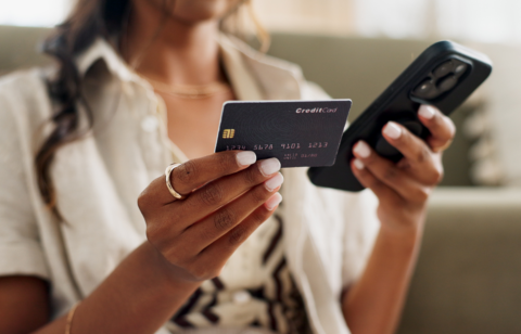 Woman holding a credit card in one hand and a smartphone in the other, possibly making an online purchase.