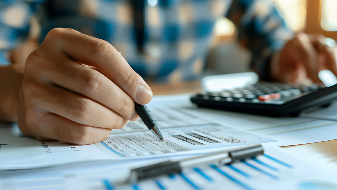 Close-up of a person analyzing financial documents with a pen and calculator.