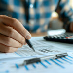 Close-up of a person analyzing financial documents with a pen and calculator.